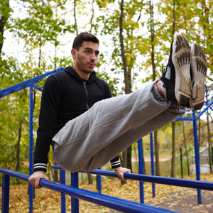 Handsome bearded man doing triceps dips on parallel bars while having outdoor workout, full-length portrait